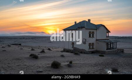 Edificio abbandonato al tramonto nella vecchia città mineraria dei diamanti di Kolmanskop vicino a Luderitz, deserto del Namib, Namibia. Foto Stock