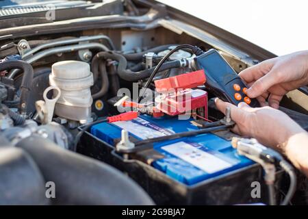 Un uomo esegue la diagnosi della batteria di un'auto con un tester, primo piano. Riparazione e sostituzione della batteria. Foto Stock