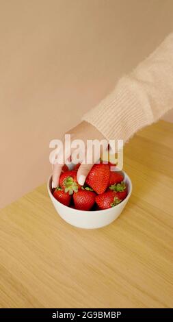 Mano di una donna che sta prendendo una fragola in una ciotola Foto Stock