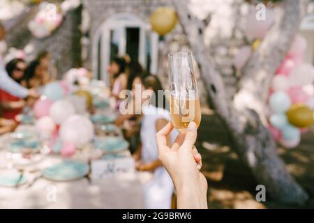 Bicchiere di champagne in mano sullo sfondo di un tavolo servito con gli ospiti Foto Stock