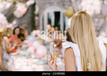 Bicchiere di champagne in mano di ragazza sullo sfondo di un tavolo servito con gli ospiti Foto Stock