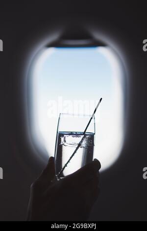 Il passeggero gusteranno un drink durante il volo. Uomo che tiene un bicchiere di gin e tonico contro la finestra dell'aeroplano. Foto Stock