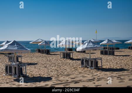Ombrelloni bianchi ripiegati e sedie a sdraio impilate in una mattinata tranquilla a Meco Beach, Portogallo. Foto Stock