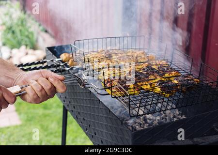 La mano ruota uno spiedino con un kebab sulla griglia Foto Stock
