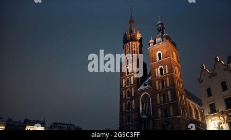 Cracovia, Polonia 03.02.2021 Vista a basso angolo della Basilica di Santa Maria, una chiesa gotica di mattoni adiacente alla Piazza del mercato principale. Alte torri gemelle contro il cielo scuro durante la notte. La città vecchia con l'architettura antica. Foto Stock