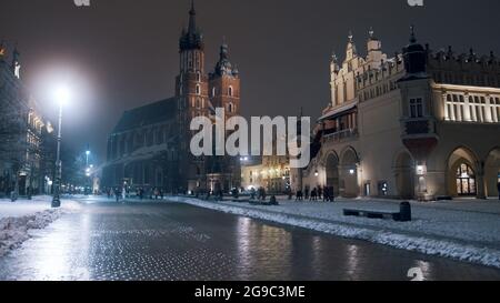 Cracovia, Polonia 03.02.2021 Vista a basso angolo di una strada bagnata nella città vecchia di Cracovia, Polonia. Basilica di Santa Maria, una chiesa gotica in mattoni adiacente alla piazza principale del mercato. Si possono vedere lanterne di strada. Riprese notturne. Foto Stock