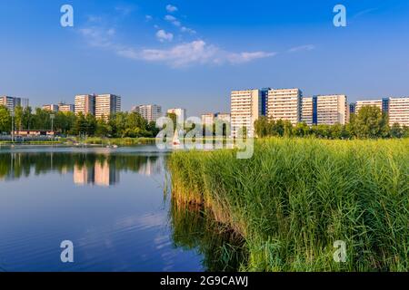 Ammira il quartiere di Tysiaclecie a Katowice in una splendida giornata di sole, vista attraverso lo stagno. Appartamenti edifici situati pulito il lago contro il cielo blu Foto Stock