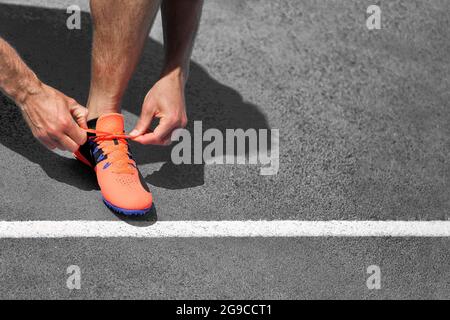 Runner man pronto a iniziare a correre su strada asfaltata legando scarpe da running lacci su sfondo grigio. Copiare lo spazio per il testo con la riga iniziale. Foto Stock