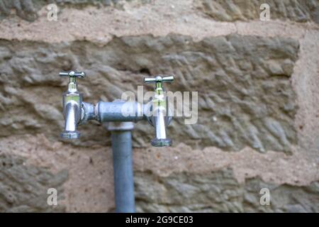 Due rubinetti in acciaio per esterni davanti ad un vecchio muro di arenaria Foto Stock