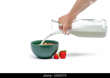 Cottura muesli, isolamento su fondo bianco Donna versa il latte da una caraffa in un piattino con fiocchi di muesli. Banner di grandi dimensioni per la stampa o la pubblicità Foto Stock