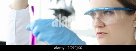 Donna chimico in occhiali protettivi gocciolando liquido rosa nel test tubo Foto Stock