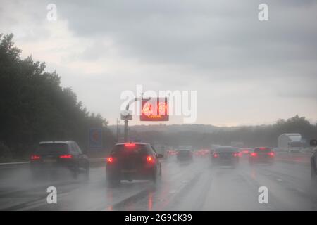 Concetto di pericoli per la strada e condizioni di guida in condizioni di bagnato - Auto che guidano lungo la strada in caso di pioggia intensa con limitazioni di velocità visualizzate sul segnale a soffitto Foto Stock