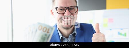 Uomo d'affari che tiene i dollari nelle sue mani e mostrando il pollice in su. Lavoro riuscito sul concetto del Internet Foto Stock
