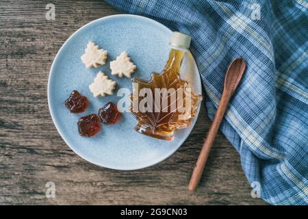 Sciroppo d'acero vista dall'alto di prodotti naturali biologici dal Canada. Bottiglia a forma di foglia d'acero, caramelle morbide e caramelle dure su rustico tavolo da cucina in legno Foto Stock