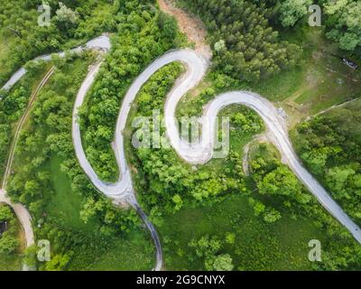 Vista sul drone della bellissima strada a serpentina che conduce attraverso il paesaggio montano in estate. Fotografia aerea di una foto di strada con un drone. Strada danneggiata Foto Stock