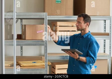 Ritratto in vista laterale di un giovane uomo che utilizza un tablet digitale in magazzino durante l'inventario e la gestione delle piccole imprese, spazio di copia Foto Stock