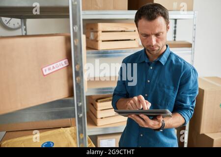 Ritratto in vita di un giovane uomo che usa un tablet digitale in magazzino mentre fa l'inventario e la gestione delle piccole imprese, spazio di copia Foto Stock