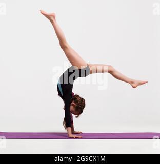 Cute bambino ragazza facendo esercizi ginnici contro bianco. Foto Stock