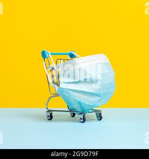 Carrello o carrello con maschera medica protettiva contro il coronavirus. Acquisto sicuro e online sul concetto di quarantena. Sfondo giallo brillante Foto Stock