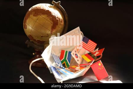 Una collezione di bandiere internazionali all'interno di una maschera di sicurezza covid con il globo di stile olden giorni sullo sfondo. Cina prominente bandiera nazionale cinese Foto Stock