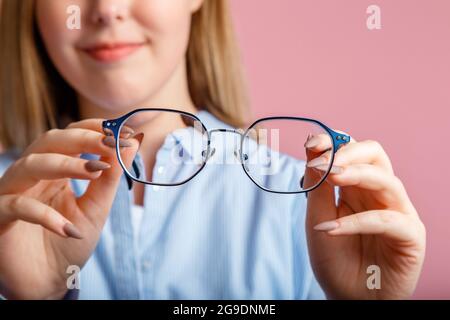 Occhiali nelle mani. Occhiali in metallo blu alla moda per la visione nelle mani femminili. Controllo della salute degli occhi, correzione della vista tramite occhiali di colore rosa Foto Stock