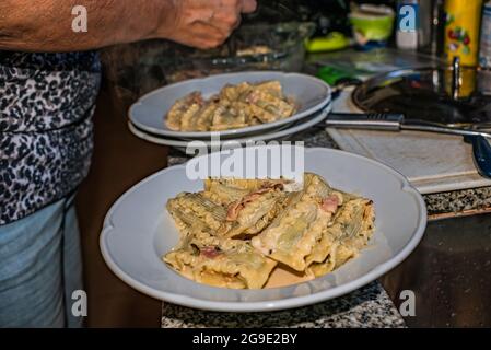 Donna che cucina pasta italiana fatta in casa, tagliatelle ripieni di spinaci e ricotta con salsa con panna, cipolle, aglio, prosciutto, spezie aromatiche e parmesa Foto Stock