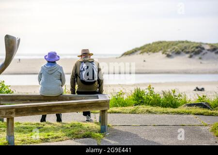 Una donna anziana e un uomo di coppia riposano dopo aver camminato mentre si siede su una panchina vicino all'Oceano Pacifico, inalando aria di mare fresca per migliorare il lavoro di Foto Stock