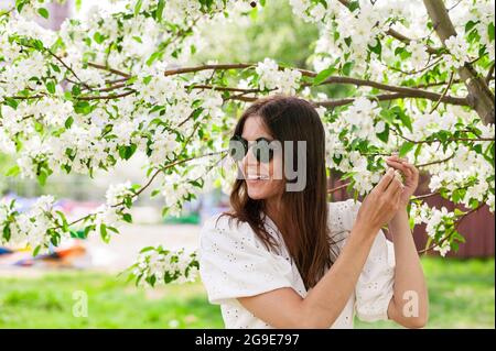 Bella giovane donna in occhiali da sole. Giovane donna etnia caucasica. Femmina sorridente e felice sta posando in abiti bianchi. Allegro pre Foto Stock