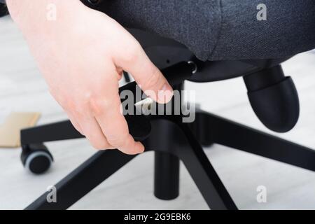 L'uomo controlla il meccanismo di sollevamento della sedia. Montaggio della sedia da ufficio all'interno Foto Stock