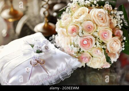 Due anelli di nozze d'oro esposti su cuscino bianco con elegante bouquet nuziale di rose rosa decorate con gemme sfaccettate in un amore, impegno e rom Foto Stock