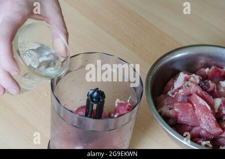 Preparazione graduale del prosciutto tagliato in casa. Fase 5: La mano versa l'acqua dal bicchiere nel miscelatore. Foto Stock