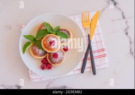 Concetto di cucina russa e Ucraina. Frittelle di formaggio cottage. Cheesecake con lampone e menta su un piatto. Foto Stock