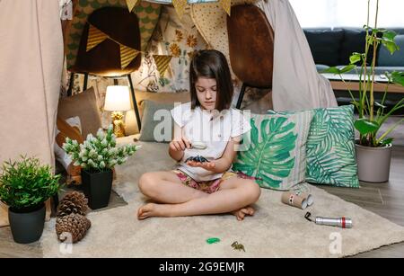 Ragazza che gioca osservando bug giocattolo con una lente di ingrandimento Foto Stock