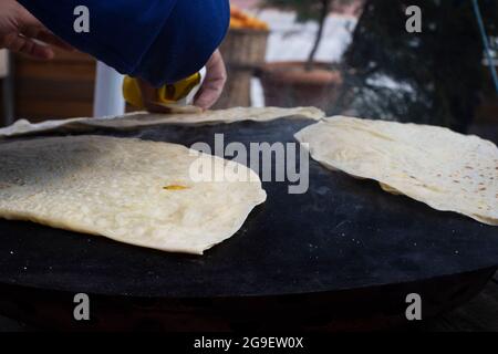 cibo di strada: pancake. donna locale cuoce pancakes su lamiera, in cui mette formaggio, spinaci, o patate. Focalizzazione selettiva. Foto Stock