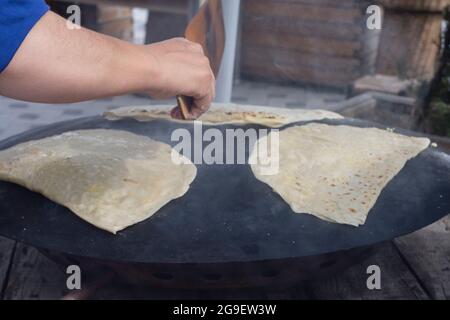 cibo di strada: pancake. donna locale cuoce pancakes su lamiera, in cui mette formaggio, spinaci, o patate. Focalizzazione selettiva. Foto Stock