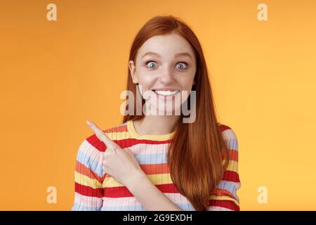 Eccitata entusiasta buon-osservante giovane ragazza silly rossa sorprende gli occhi pop la telecamera ha impressionato puntando l'angolo in alto a sinistra vedere super star grinning Foto Stock