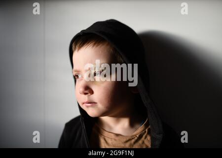 Povero ragazzo triste con sopracciglia tagliata in piedi in casa, concetto di povertà. Foto Stock