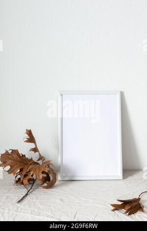 Casa decoratore moccap, quadro vuoto cornice vicino bianco dipinto muro di cemento, rami con foglie asciutte Foto Stock
