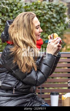 Giovane donna affamata mangia Burger e si prende pausa pranzo all'aperto nel Park.fast food. Concetto di cibo da asporto. Foto Stock