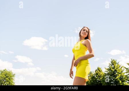 Abito giallo stile estivo. Indossate una donna slim-fit alla moda, il cielo blu e le nuvole sullo sfondo. Benessere, buon umore. Foto Stock