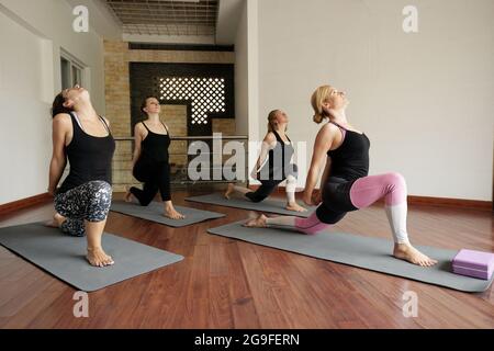 Le donne che frequentano la lezione di yoga indoor e che fanno il affondo crescente basso pongono che coinvolgono molti muscoli Foto Stock