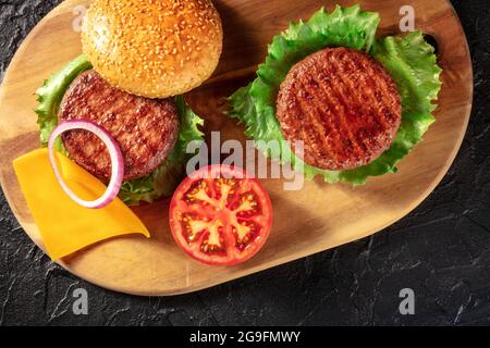 Ingredienti Burger su sfondo nero. Hamburger fatti in casa con polpettine di manzo, foglie di insalata verde, cipolla rossa, pomodoro e formaggio Cheddar Foto Stock