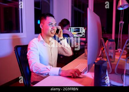 Allegro sviluppatore di software sorridente quando risponde a una chiamata telefonica del cliente da un fuso orario diverso Foto Stock