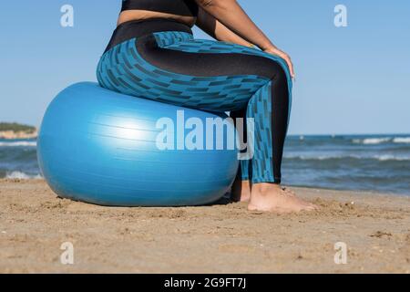 Vista closeup donna durante esercizi di yoga fitness utilizzando palla fitness sulla spiaggia Foto Stock