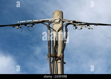 Parte superiore del palo per utenze elettriche in calcestruzzo con vari fili elettrici neri collegati con piccoli isolatori in ceramica sul retro del cielo blu nuvoloso Foto Stock