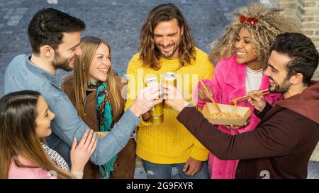 Gruppo multirazziale di giovani felici che si divertono per strada celebrando l'amicizia tostando con bevande in scatola. I Millennial che si riuniscono bevendo essere Foto Stock