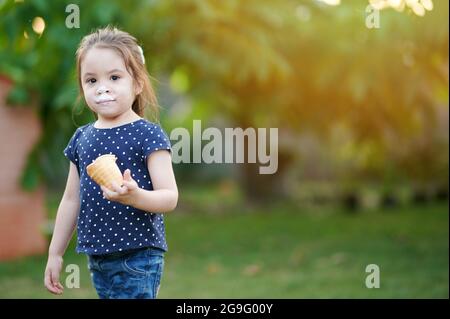 Ragazza tenere il cono gelato su sfondo verde sfocato parco Foto Stock