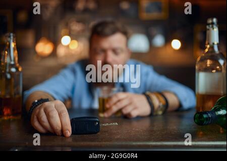 Uomo ubriaco con la chiave dell'auto seduta al bancone del bar Foto Stock