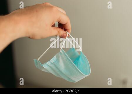 Mano della donna che tiene una maschera chirurgica usata Foto Stock
