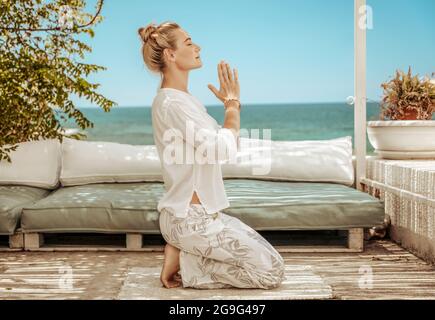 Bella calma femmina fare esercizi di yoga sulla terrazza della Beach House. Meditare sulla spiaggia. Armonia dell'anima. Vacanza estiva tranquilla. Foto Stock